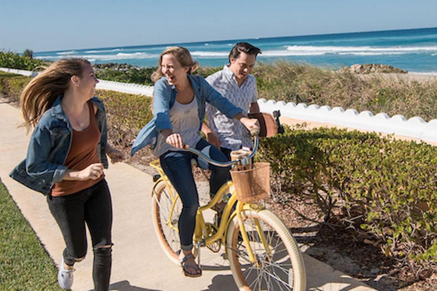 三名PBA学生, 拿着滑板的人, 骑自行车的人, 一个人走路, 在海滩附近的一条小路上.